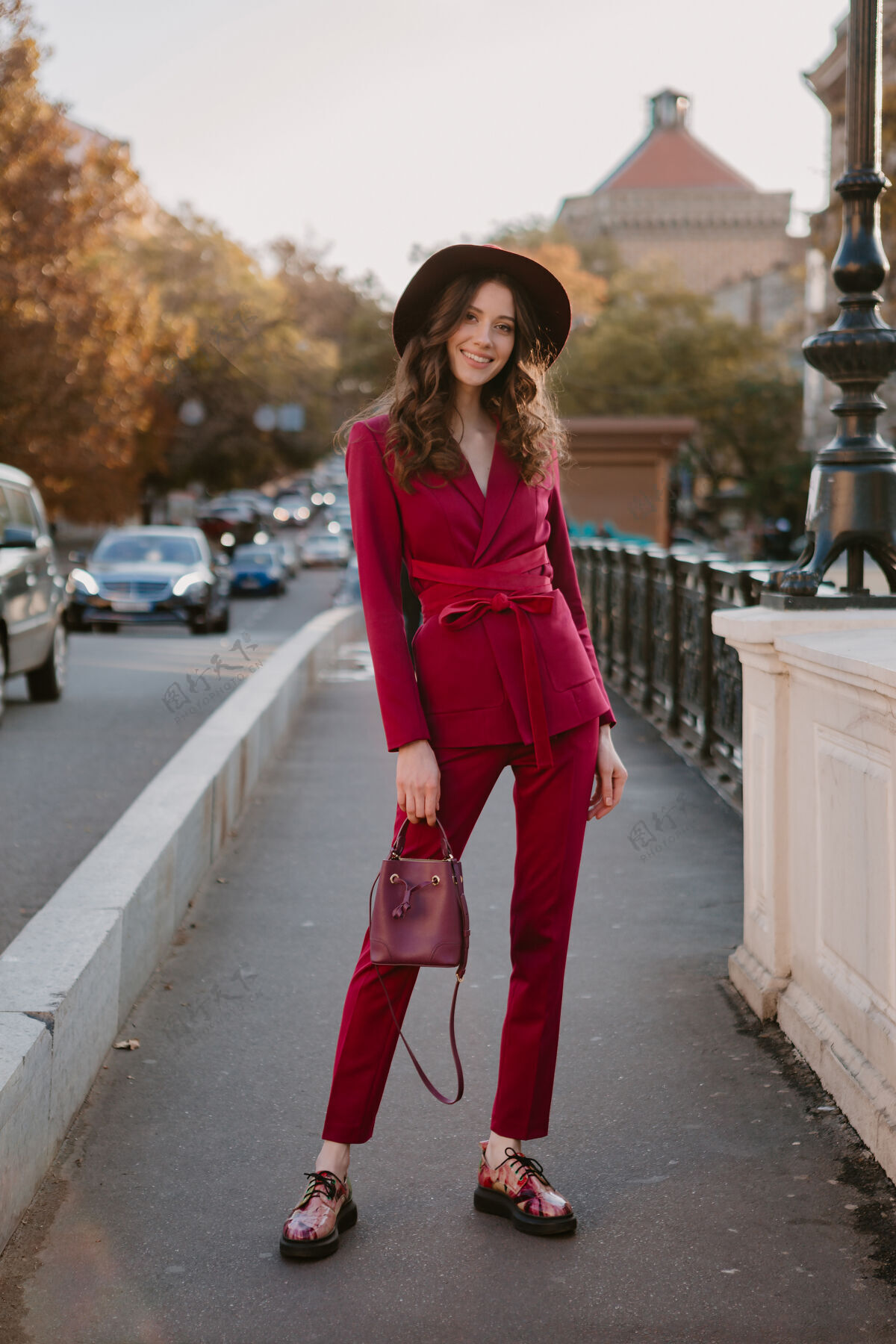 年轻穿着紫色西装的漂亮时髦女人走在城市街头 春夏秋冬时节时尚潮流戴着帽子 手拿钱包秋天配饰深色