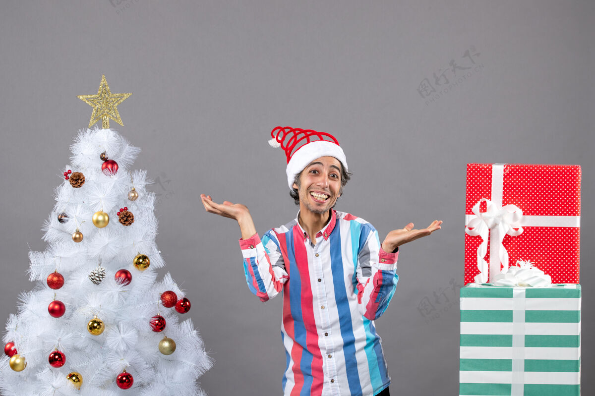 男性正面图快乐的年轻人张开双手站在白色圣诞树旁站立圣诞打开