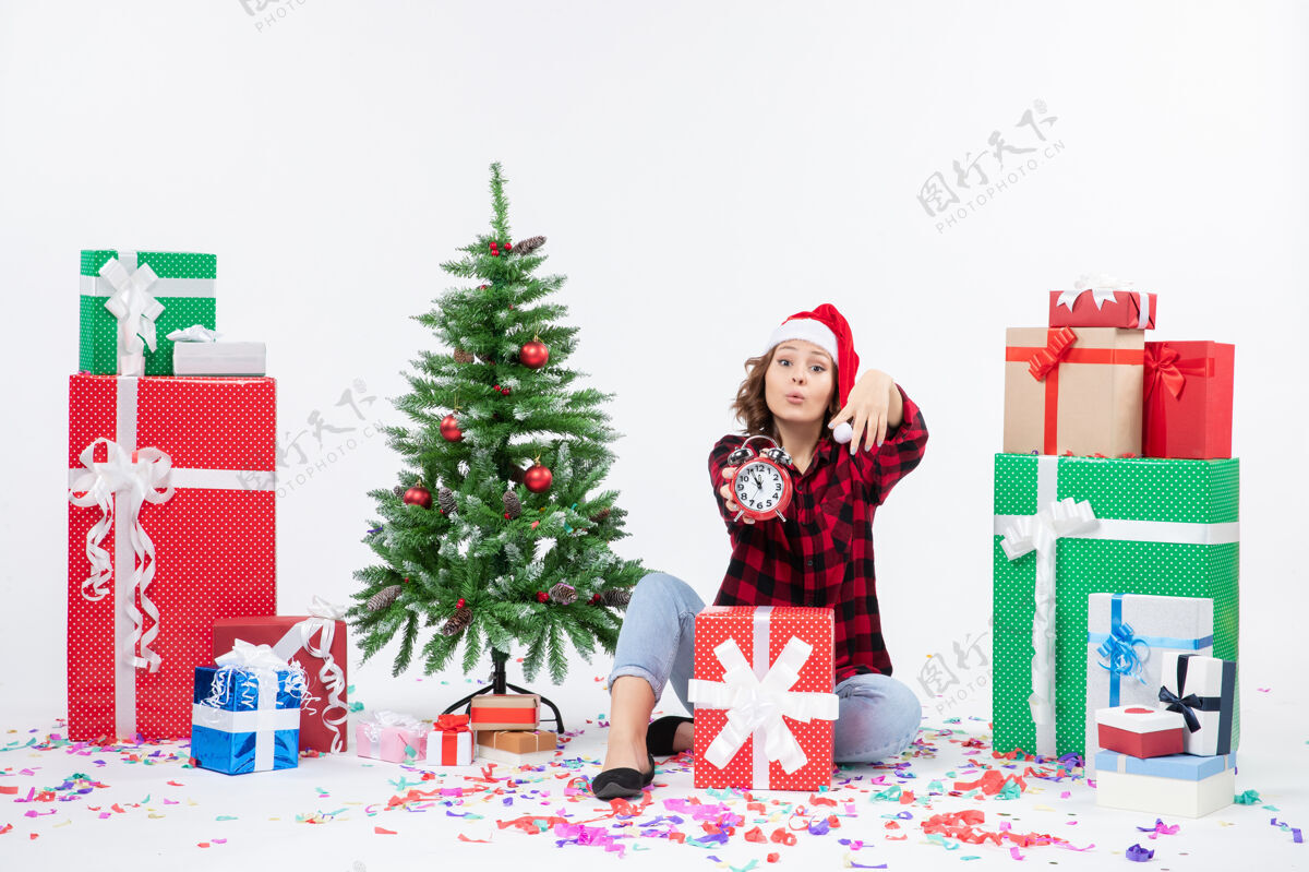 礼物前视图的年轻女子坐在圣诞礼物周围拿着白色墙上的时钟礼物圣诞雪