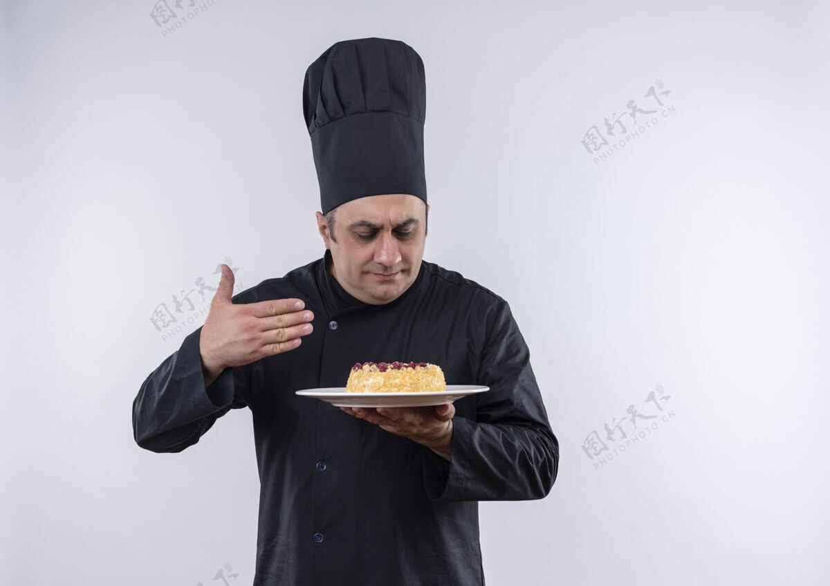 手一位身穿厨师制服的中年男厨师闭着眼睛嗅着盘子里的蛋糕盘子蛋糕制服
