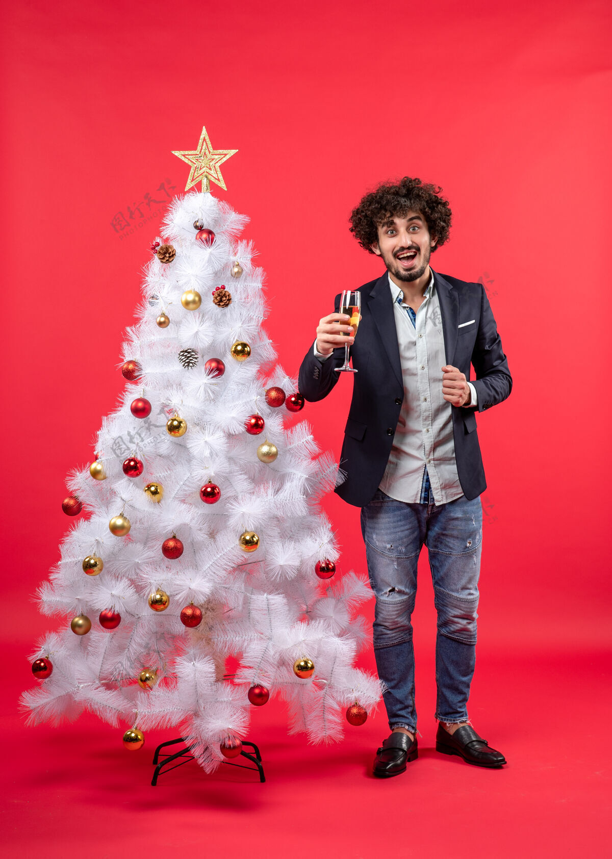 新年前夜圣诞树旁站着一个留着胡须的快乐的年轻人 手里拿着酒庆祝圣诞快乐成人圣诞老人