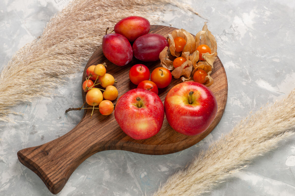 顶部顶视图不同形状的李子酸和新鲜水果与红苹果放在浅白的桌子上水果苹果新鲜