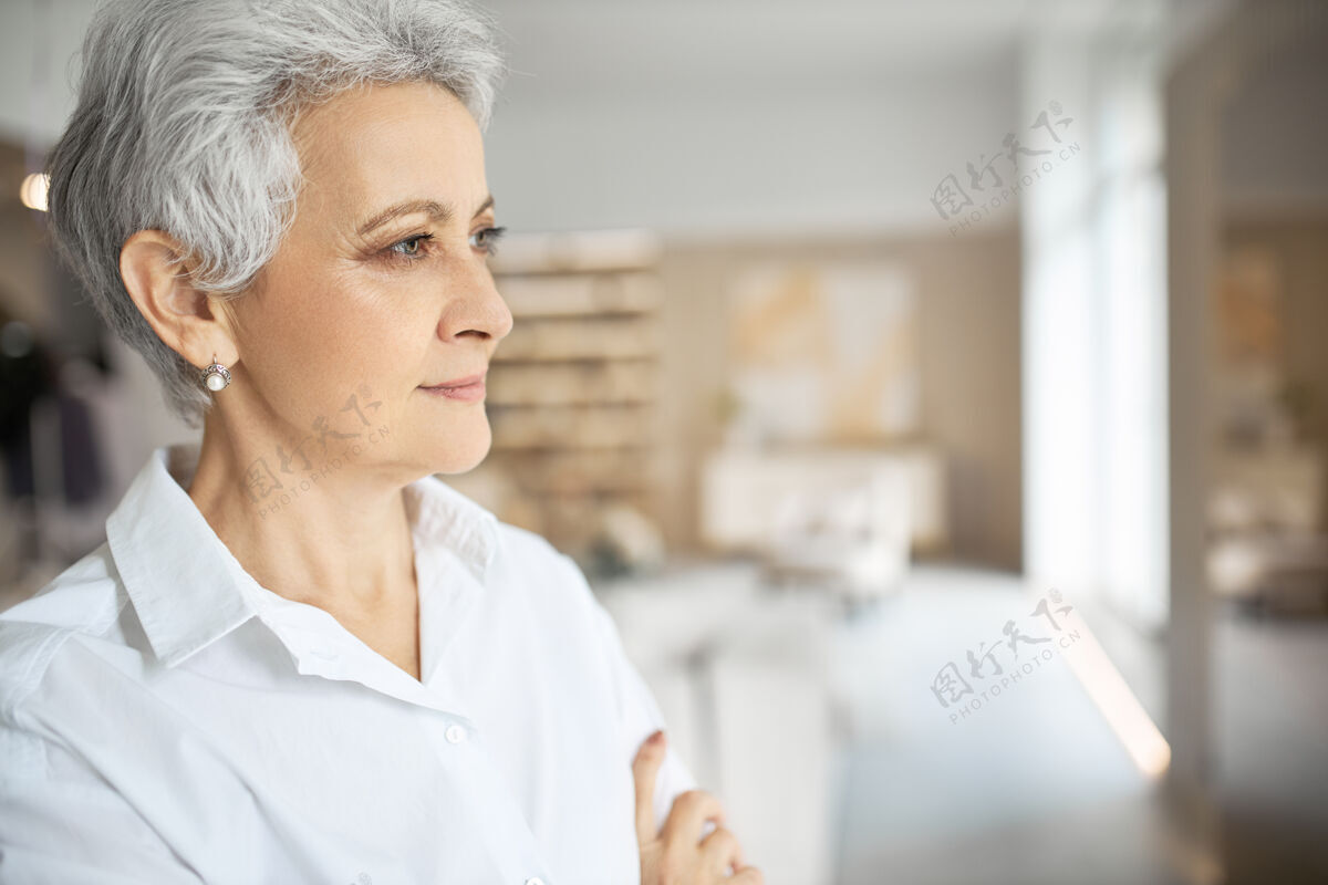退休优雅时尚的成熟女企业家穿着白色正式衬衫站在现代办公室内部的资料图片开朗专业人士年龄