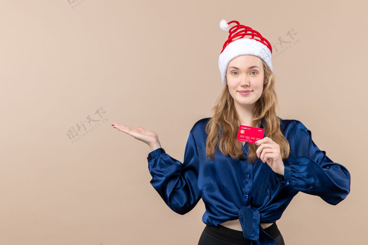 年轻正面图年轻女性手持红色银行卡上粉色背景钱过节照片新年圣诞感慨微笑年轻女性帽子