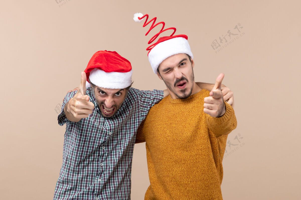 服装前视图两个热情的家伙 戴着圣诞帽 在米色的孤立背景上向你展示男性视图前面