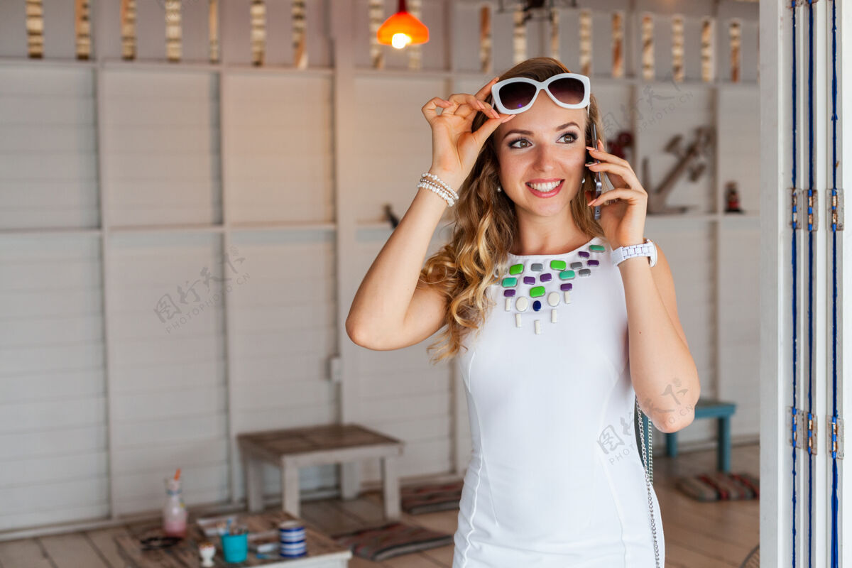 时尚在夏日咖啡馆里 一个穿着白裙子 戴着墨镜的漂亮女人在打电话衣服手机电话