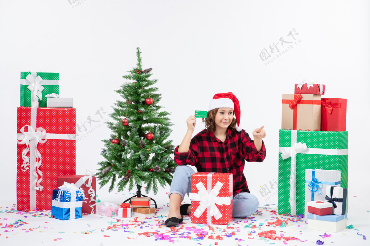快乐正面图：年轻女子围坐在白墙上 手里拿着绿色的银行卡前面礼物圣诞快乐