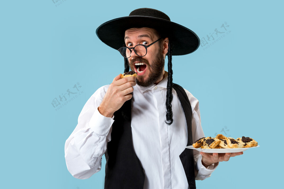 盘子这位年轻的东正教犹太男子戴着黑帽子 在犹太普瑞姆节上吃哈曼塔森饼干曲奇犹太教糕点