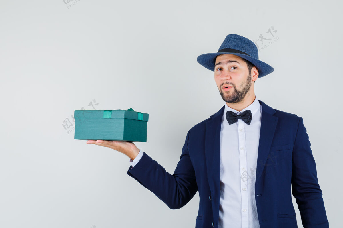 肖像穿着西装 戴着帽子的年轻人展示着礼物盒 看上去很正面 正面视图长相男人站立