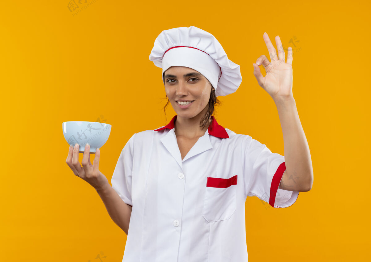 厨师面带微笑的年轻女厨师穿着厨师制服拿着碗 摆出一副很好的姿势穿着手势展示