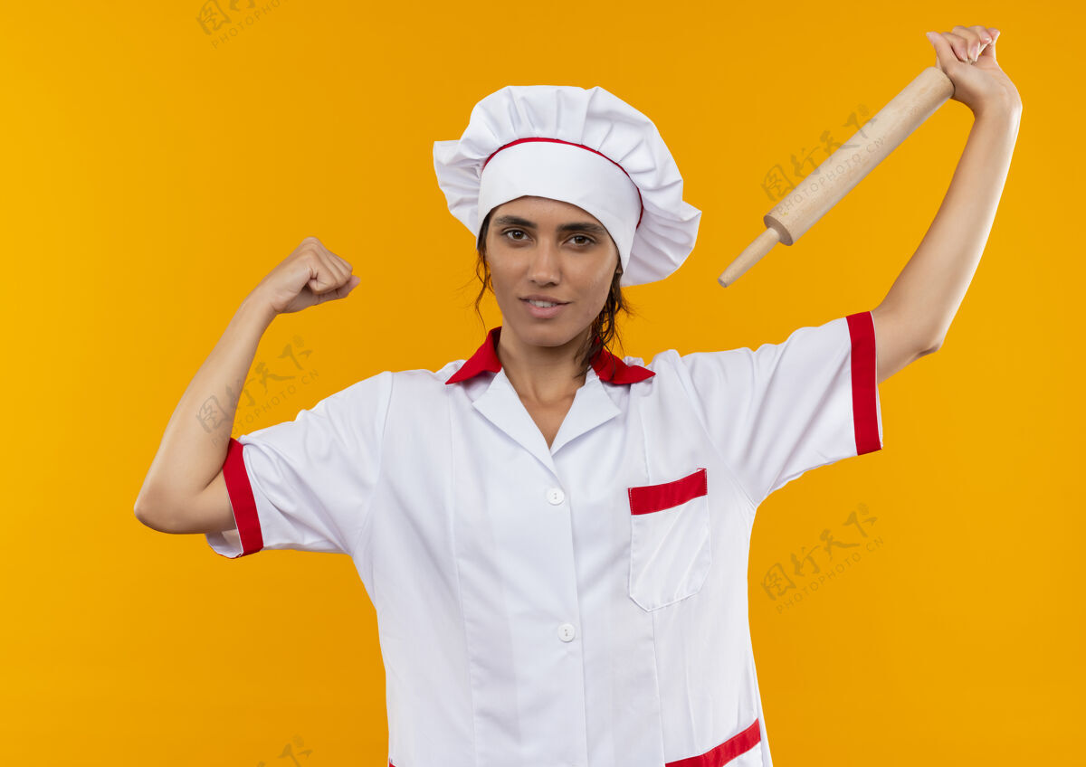 厨师高兴的年轻女厨师穿着厨师制服 肩上举着擀面杖做着坚强的手势高兴滚强壮
