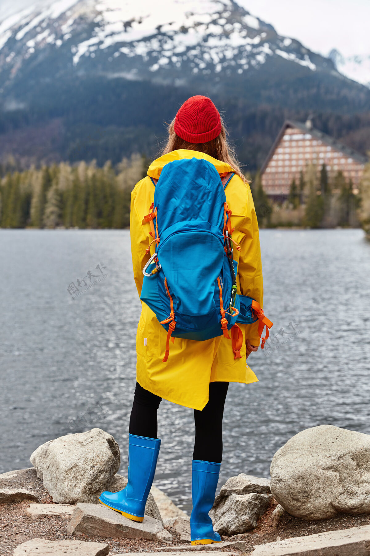 帽子垂直拍摄的女徒步旅行者享受惊人的自然景观 站在石头背对着相机山背包雨衣