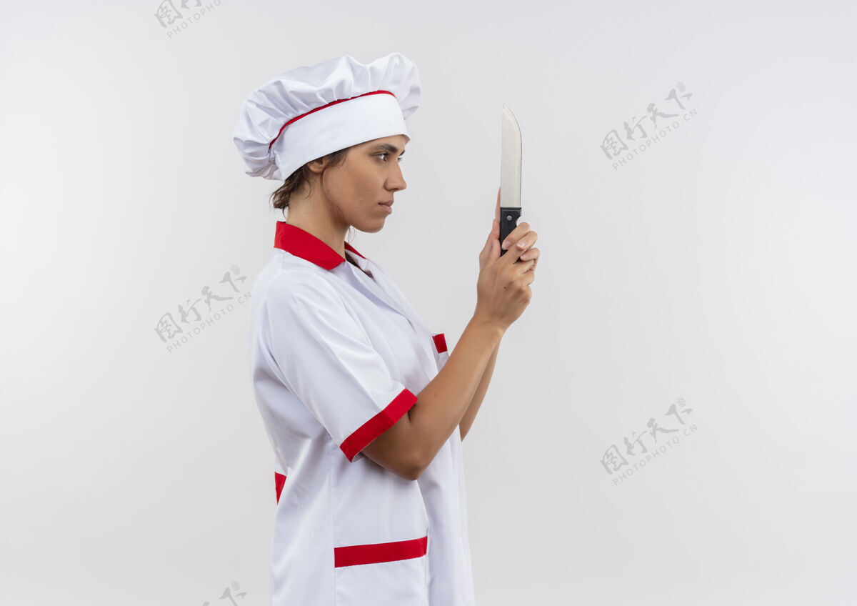 戴着站在剖面图年轻的女厨师穿着厨师制服拿着和看刀与复制空间刀制服侧面