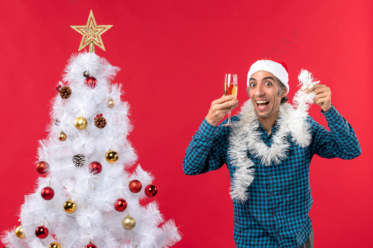 年圣诞气氛与疯狂的年轻人圣诞老人帽子和提高一杯葡萄酒欢呼自己附近的圣诞树香槟快乐年轻人
