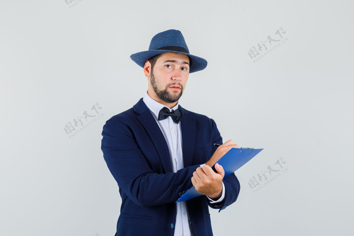 小伙子年轻人穿着西装 戴着帽子 在剪贴板上做笔记 看起来很理智 正面视图手肖像剪贴板