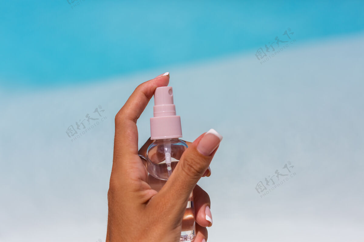 椰子手拿着一小瓶晒黑油液在蓝色的游泳池上方保护特写护理