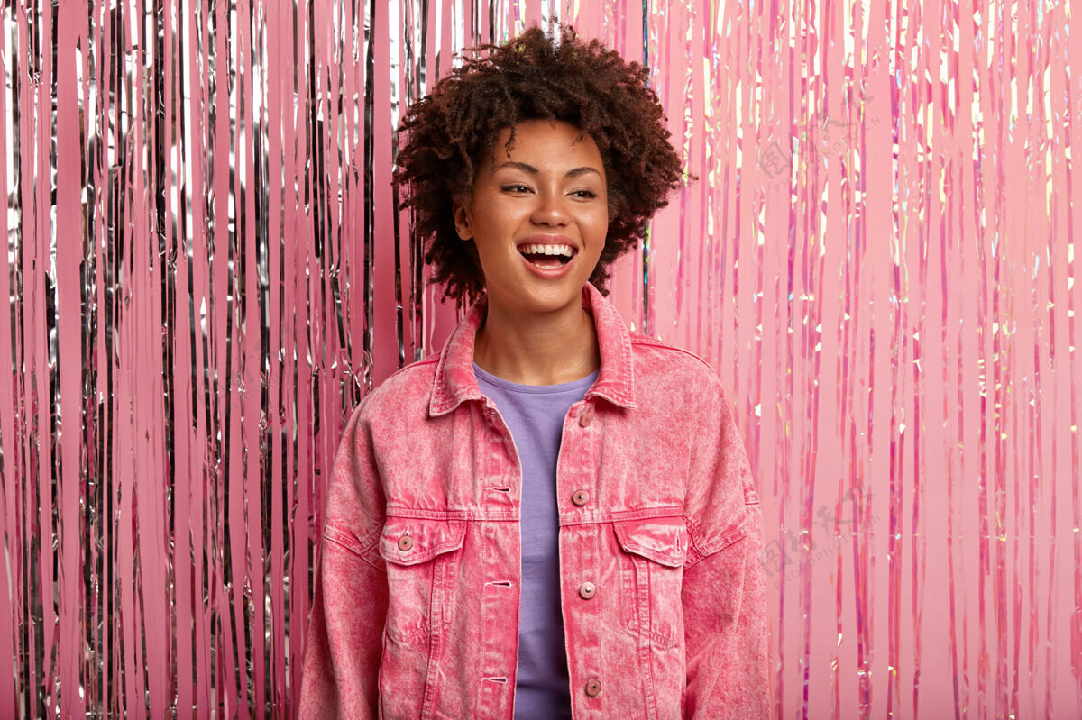 人类年轻微笑的非洲裔美国女性 妆容微薄 穿着粉色夹克时尚卷曲凝视