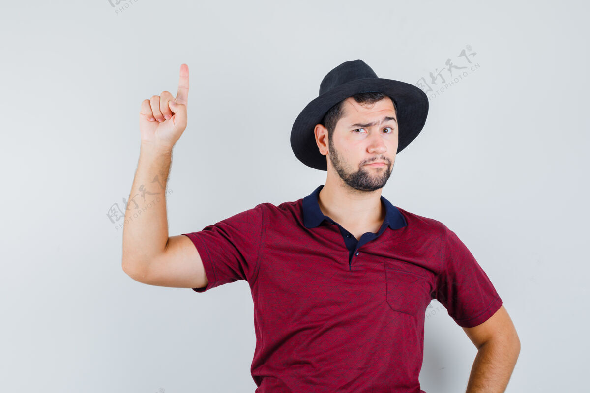 肖像年轻人指着红t恤衫 戴着帽子 看上去很困惑前视图英俊向上友好