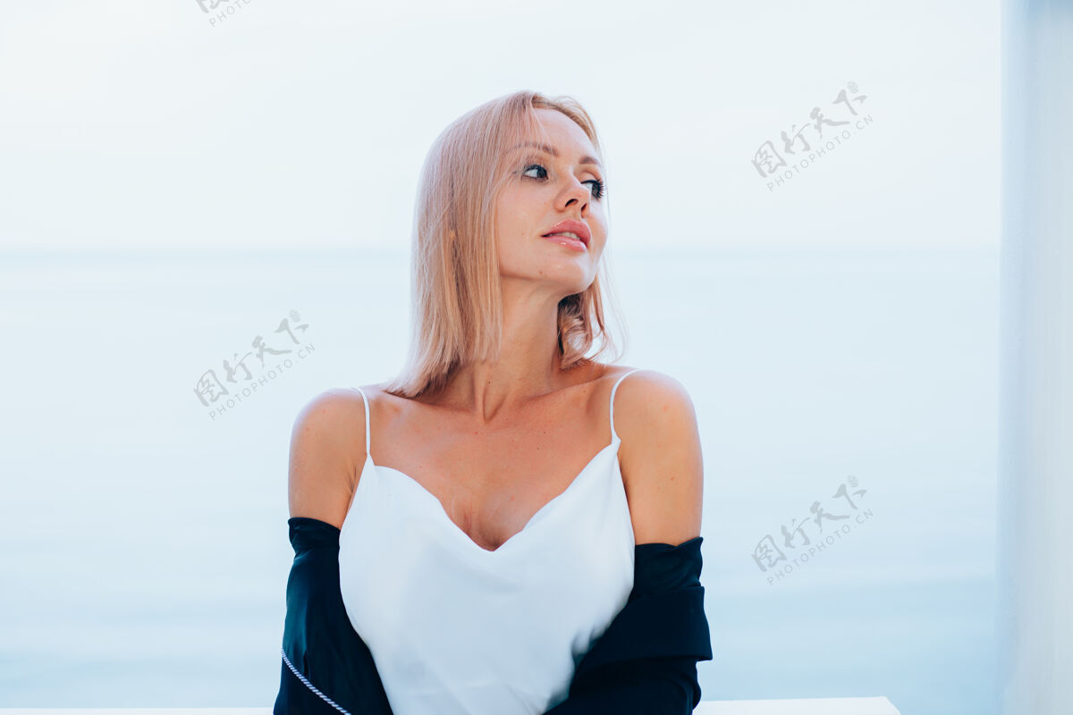 时尚时尚写真时尚的白种女人在丝绸长裙黑色外套豪华的地方与海景衬衫站立白色连衣裙