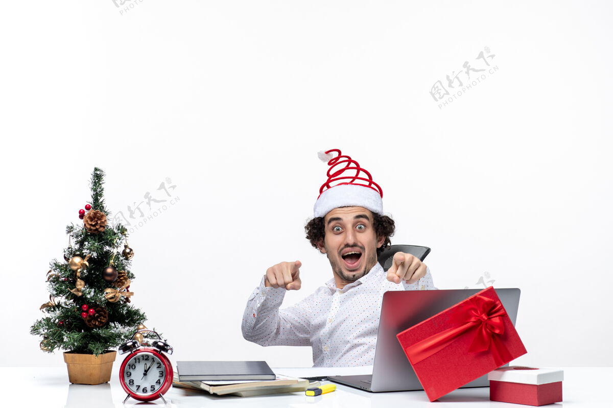 笔记本电脑新年的心情和微笑兴奋的年轻商人坐在办公室里 指着白色背景上的东西指着人年轻的商人