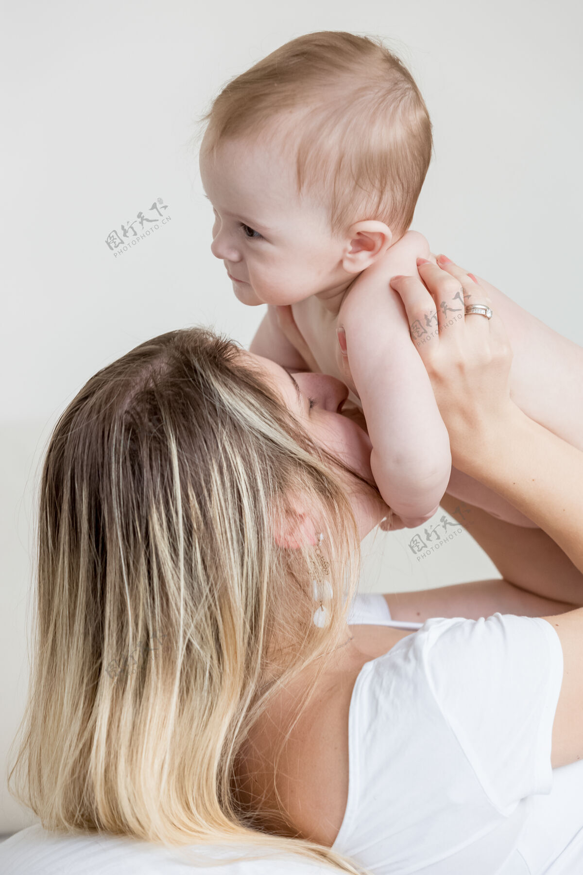 玩特写照片 年轻的母亲亲吻和玩她的9个月大的男婴年轻抱着室内